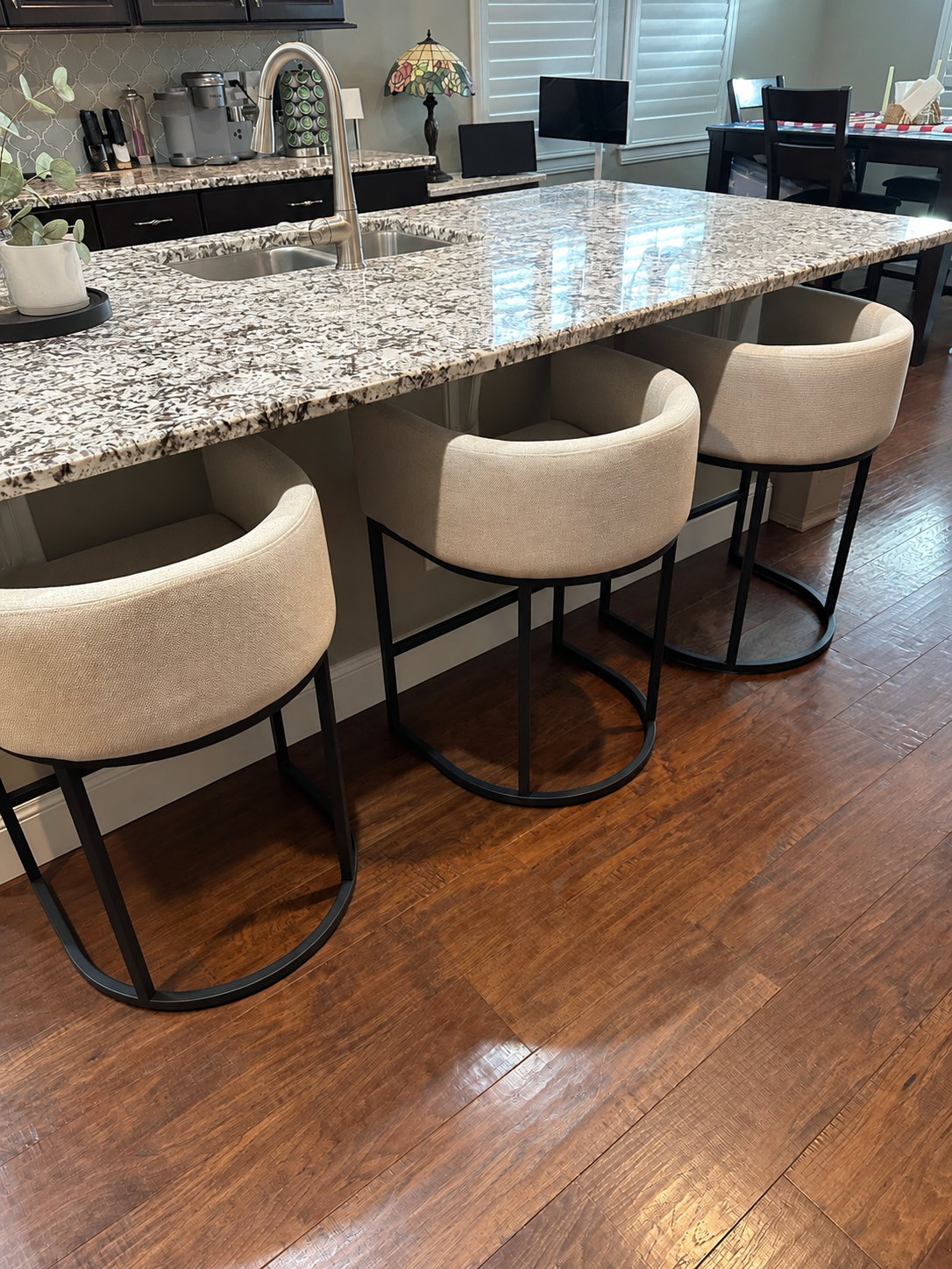 Three beige curved-back counter stools with black metal bases at Rose’s kitchen island. Photo background tidied with AI.